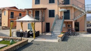 A two-story building with a balcony, outdoor seating area, and a staircase leading to the upper floor. - Casa Vacanze La Fonda (Santo Stefano di Magra)
