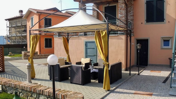 An outdoor seating area with a covered patio, wicker furniture, and a stone wall. - Casa Vacanze La Fonda (Santo Stefano di Magra)