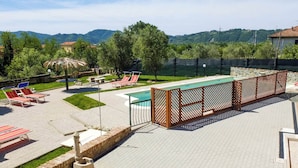 A pool area with lounge chairs, a wooden fence, and a view of hills in the background. - Casa Vacanze La Fonda (Santo Stefano di Magra)