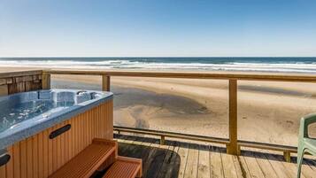 Eine Holzterrasse mit Whirlpool und Sitzgelegenheit mit Blick auf einen Strand.