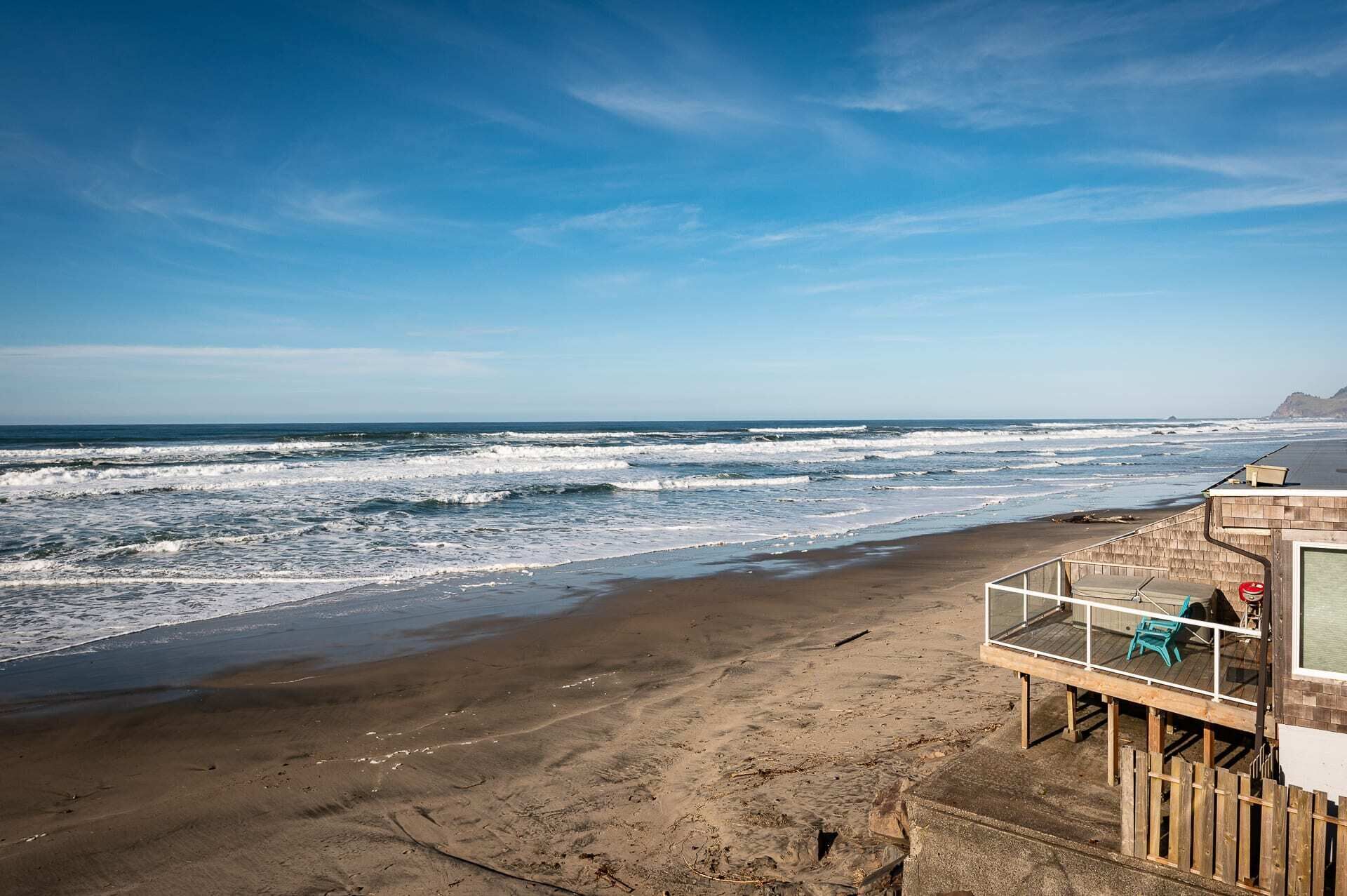 Vista a la playa con una terraza de madera y una silla, con vista al océano.