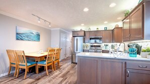 Una cocina moderna con gabinetes de madera, electrodomésticos de acero inoxidable y una zona de comedor con sillas y una mesa de madera.