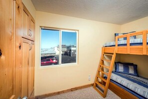 Une chambre avec un lit superposé, une armoire en bois et une fenêtre donnant sur un parking.