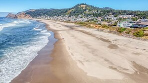 Una spiaggia costiera con una riva sabbiosa, alcuni edifici sullo sfondo e un paesaggio collinare.