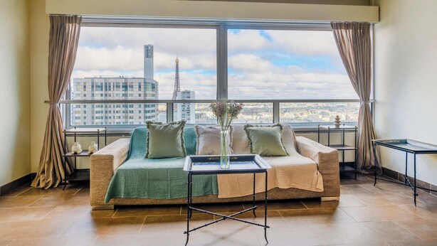 Uma sala de estar moderna com uma janela grande, um sofá, uma mesa de centro e vista para o horizonte urbano.