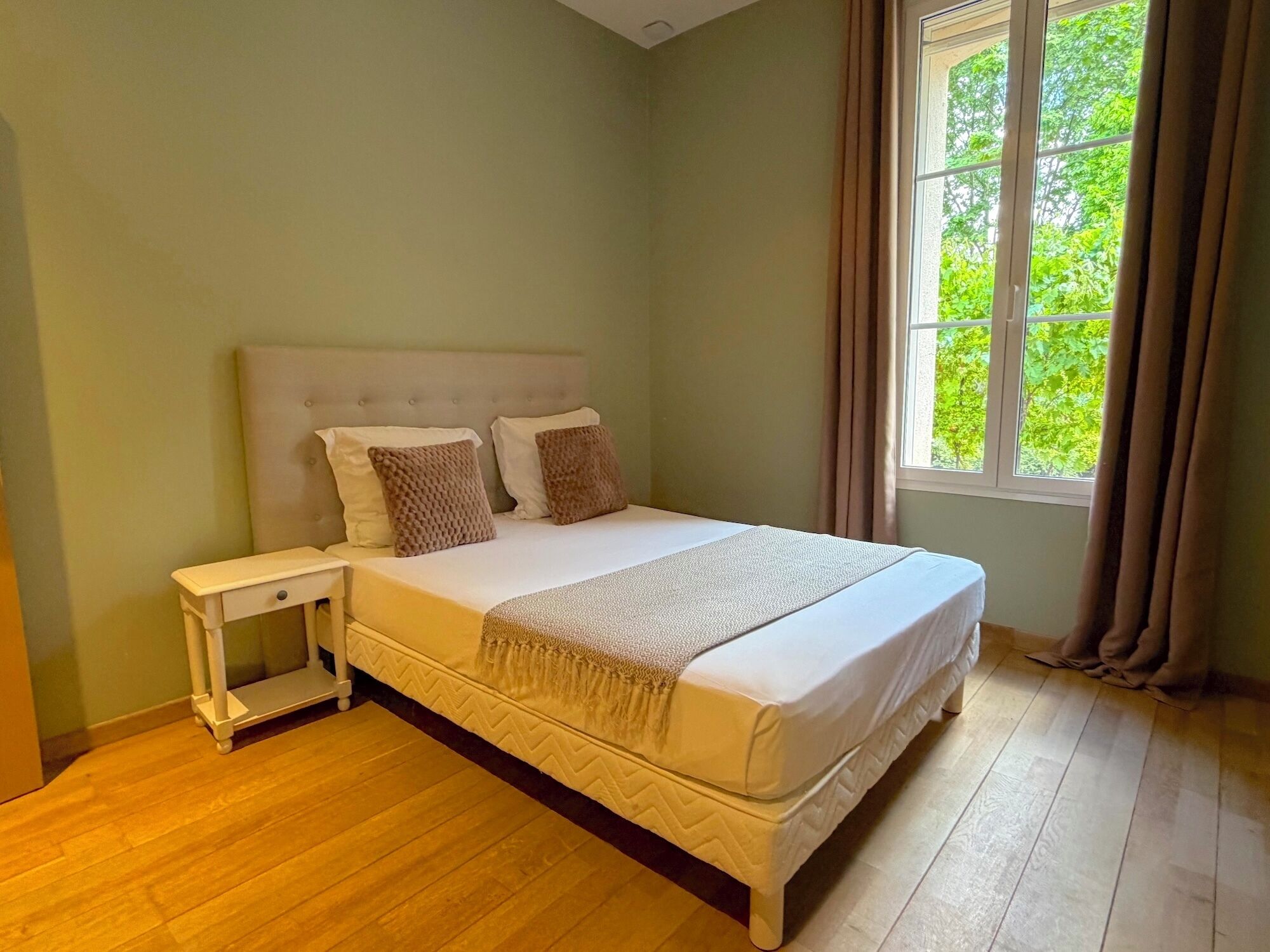 A bedroom with a bed, nightstand, and window with curtains.
