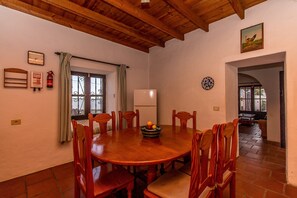 A dining room with a wooden table and chairs, a fire extinguisher, a clock, and a window with curtains.