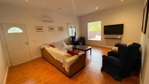 Ein geräumiges Wohnzimmer mit Sofa, Sessel und einem an der Wand befestigten Flachbildfernseher.