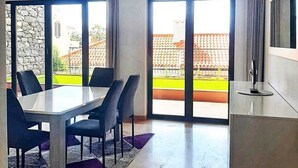 Un espace de restauration moderne, avec une table et des chaises, de grandes fenêtres et une vue sur un bâtiment doté d’un toit en tuiles.