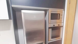 Une cuisine compacte équipée d’un réfrigérateur en acier inoxydable, d’un four à micro-ondes et d’un four encastré.