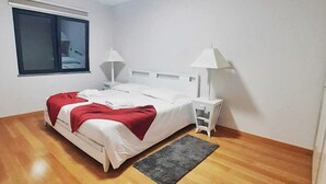 Une chambre à coucher avec un lit, deux lampes de chevet, une fenêtre et un petit radiateur.