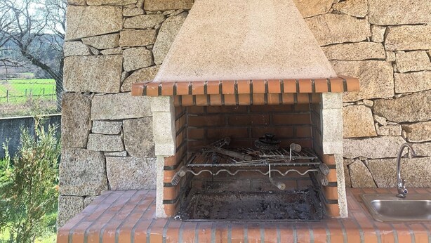 A stone-built outdoor fireplace with a brick base and a chimney, set in a wooden structure with a sloped roof. - HYDRANGEA HOUSE (Vila Nova de Paiva)