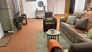 A living room with a sofa, armchair, and coffee table. There is a staircase in the background and a stone wall on the left. - HYDRANGEA HOUSE (Vila Nova de Paiva)