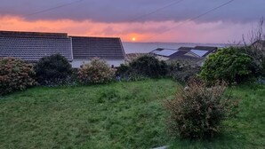 A residential area with houses, a grassy lawn, and a sunset over the sea.