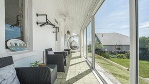 A covered outdoor area with wicker furniture, a hanging chair, and a view of a house.