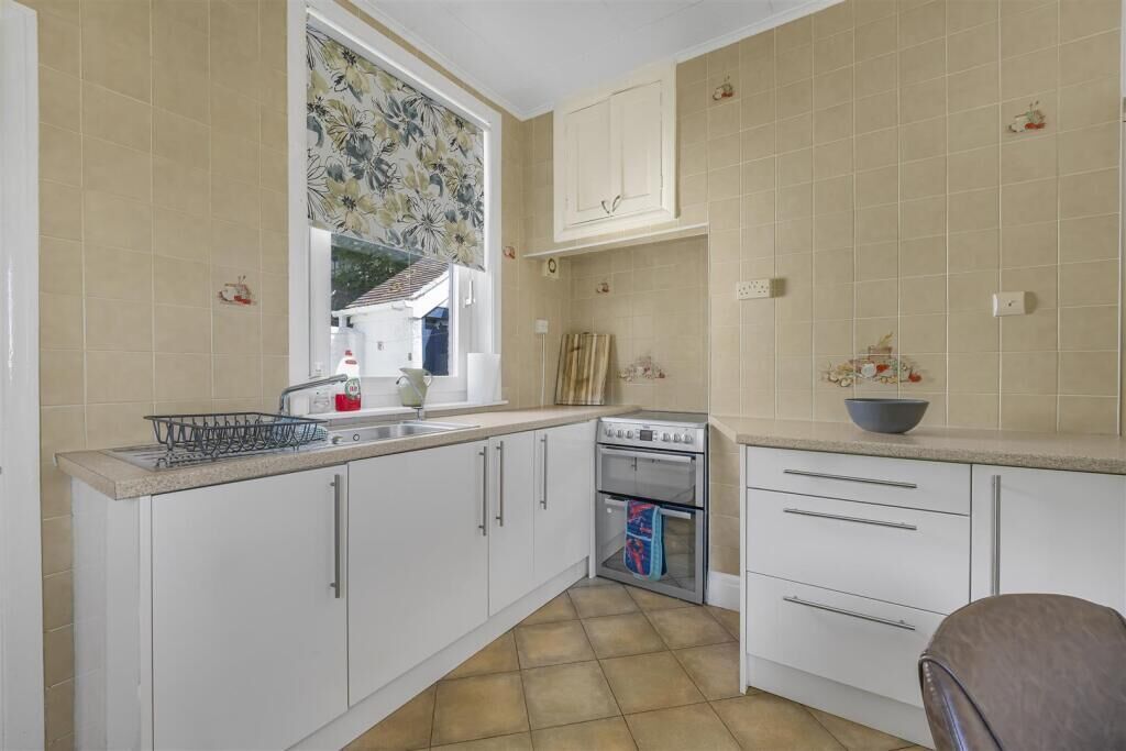 A kitchen with white cabinets, a stove, and a window with floral curtains.