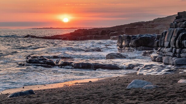 A coastal sunset with waves crashing against rock formations.