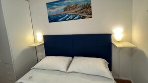 Ein Schlafzimmer mit einem Bett, zwei Nachttischlampen, einem Nachttisch und einem Bild einer Küstenlandschaft.