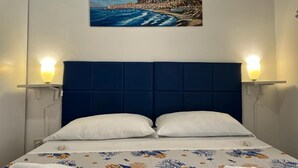 Ein Hotelzimmer mit einem Bett, weißen Kissen, einer blumigen Tagesdecke und einem Gemälde einer Küstenlandschaft über dem Bett.