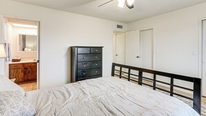 Een slaapkamer met een bed, een dressoir, een plafondventilator en een deur.