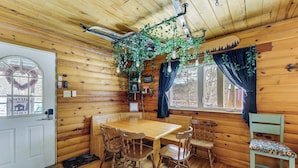 A wooden cabin interior with a dining table, chairs, a bench, a window with curtains, and a hanging plant. - Family Cabin! Close to Greenbrier River & Snowshoe (Cass)