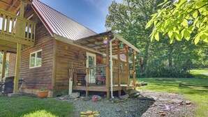 A wooden cabin with a porch, a small deck, and a garden area with rocks and a flower bed. - Family Cabin! Close to Greenbrier River & Snowshoe (Cass)
