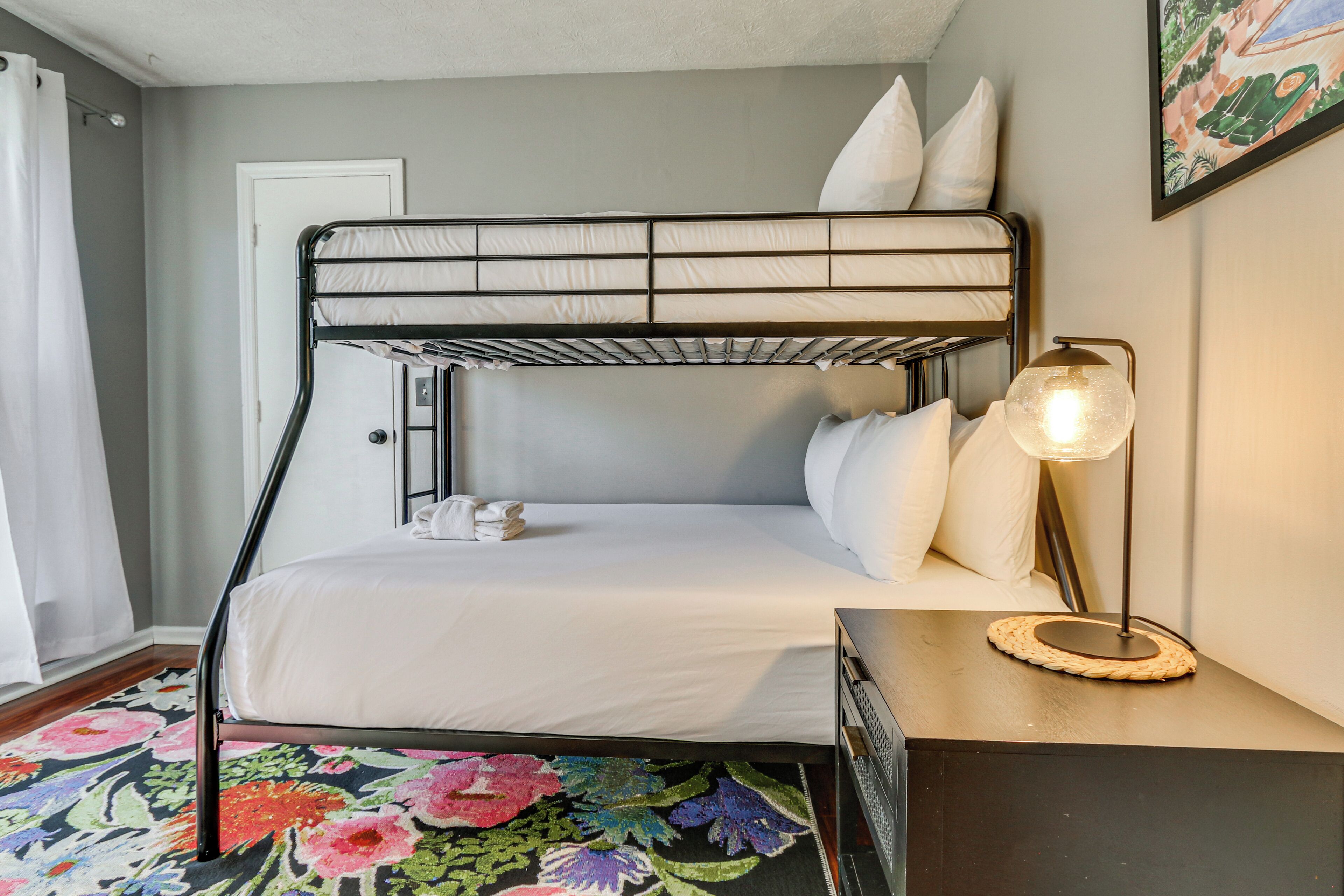 A bunk bed with white bedding, a bedside lamp, and a floral rug.