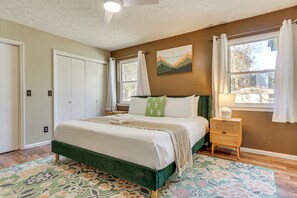 A bedroom with a bed, a nightstand, a window with curtains, a painting on the wall, and a door. - Dogs Welcome! Savannah Escape w/ Fenced-in Yard (Savannah)