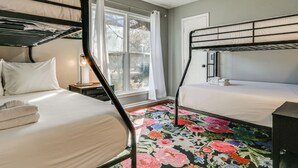 A dormitory room with bunk beds, a large window with curtains, a ceiling fan, and a floral carpet. - Dogs Welcome! Savannah Escape w/ Fenced-in Yard (Savannah)