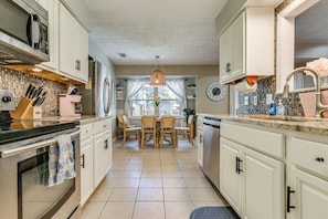 A kitchen with white cabinets, a stainless steel refrigerator, a microwave, and a dining area with a table and chairs. - Dogs Welcome! Savannah Escape w/ Fenced-in Yard (Savannah)