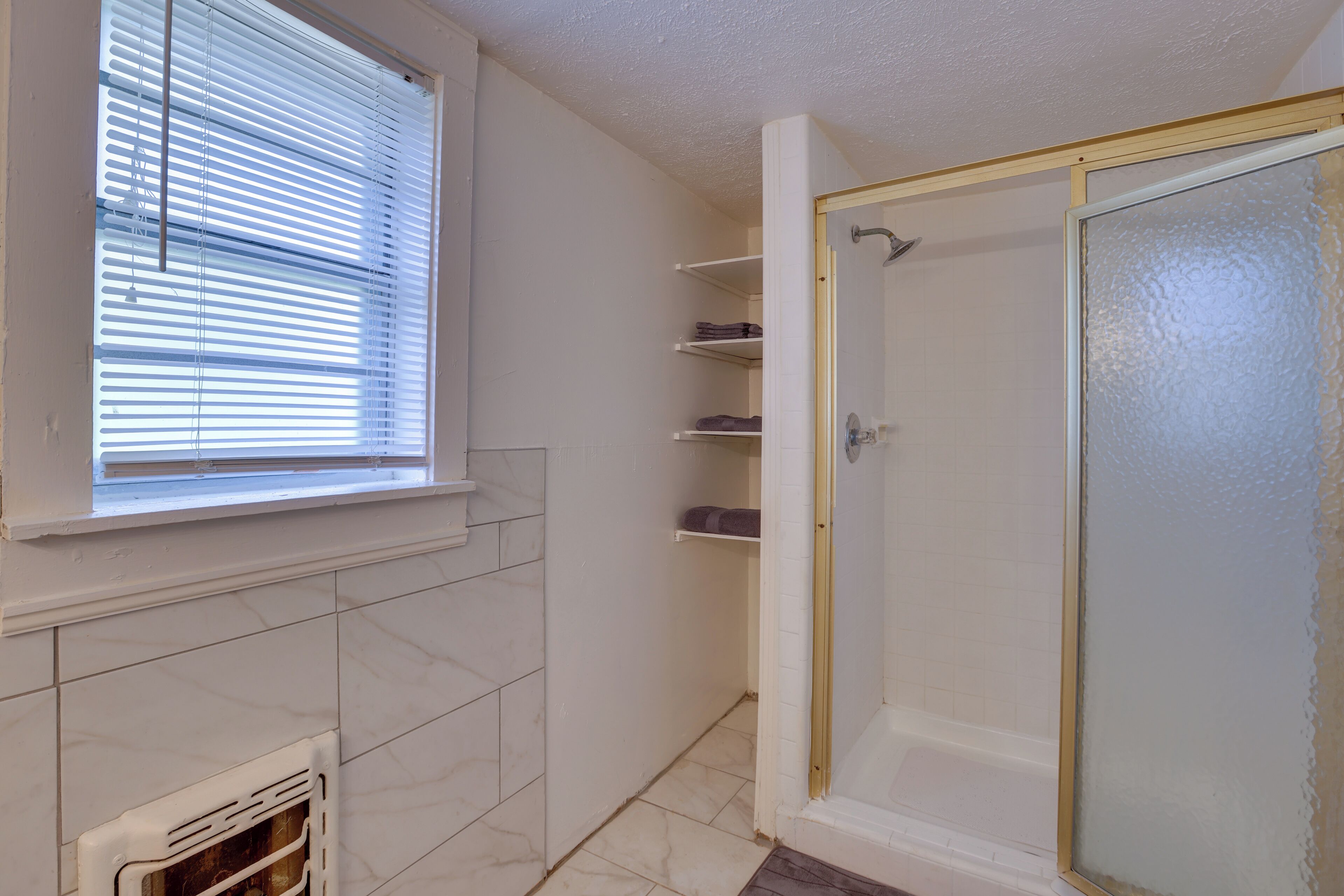Ein Badezimmer mit Fenster, Dusche und Fliesenboden.