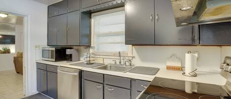 A modern kitchen with grey cabinets, a microwave, a stove, and a sink.