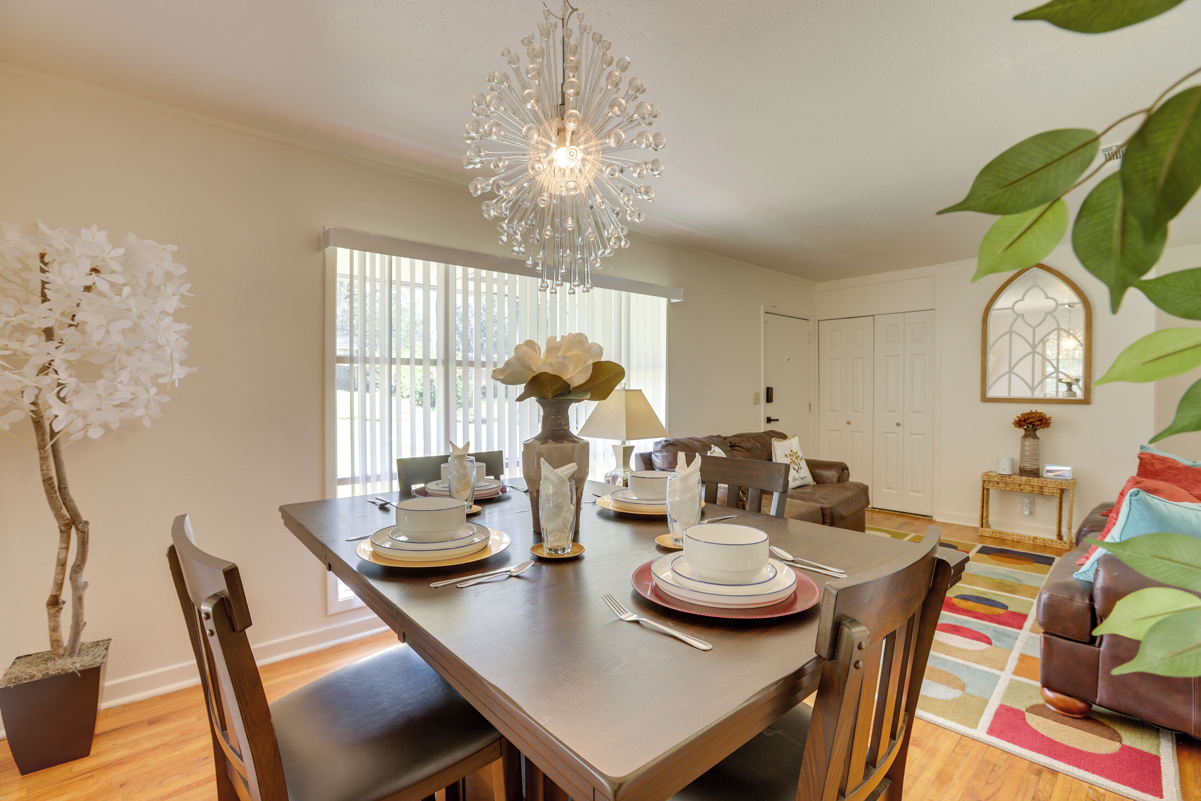 A dining area with a chandelier, white floral arrangement, and a dining table set for four.