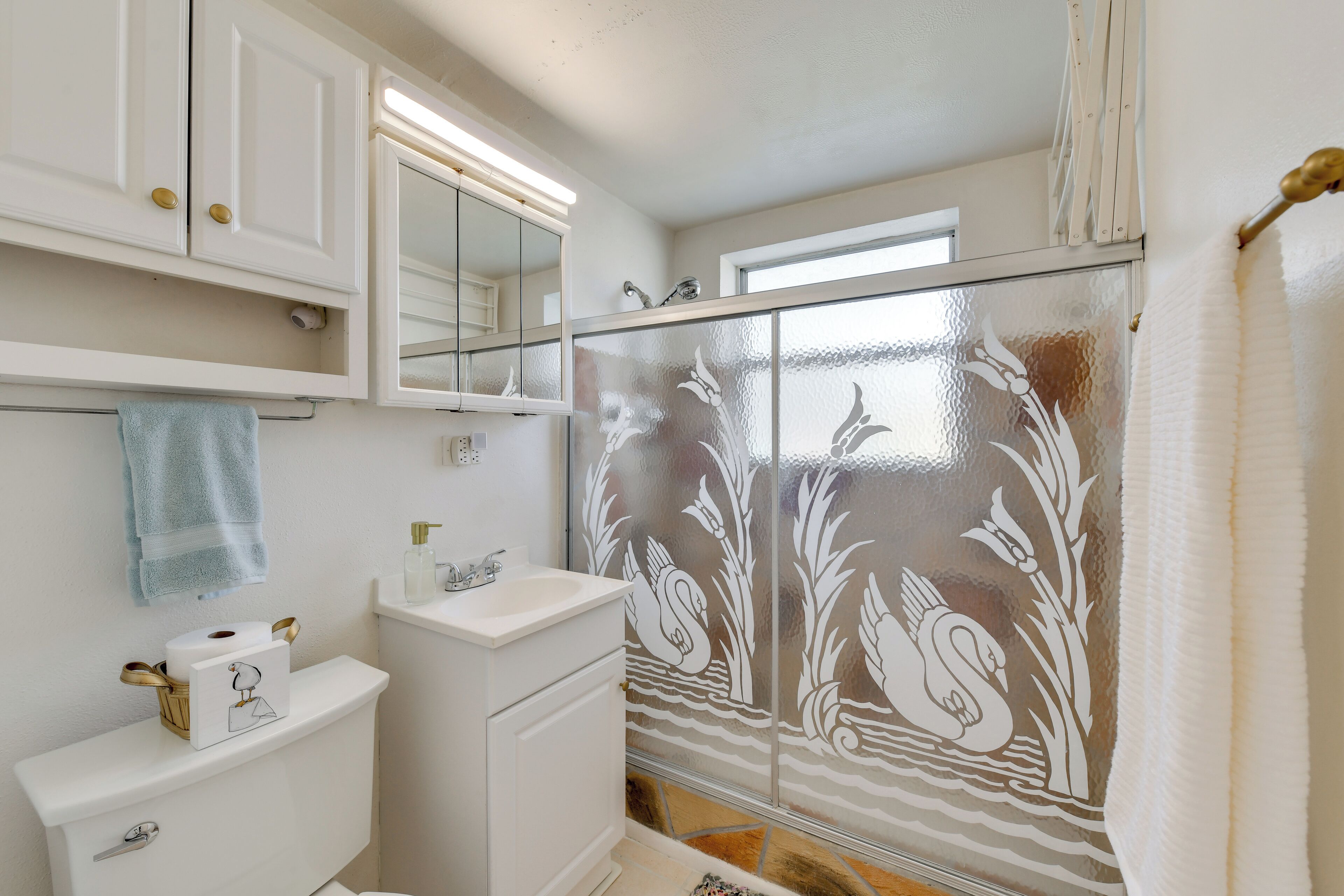 Baño con inodoro, lavabo, espejo y ducha con detalles de vidrio decorativo.