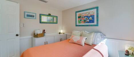 Quarto com uma cama grande, mesa de cabeceira com abajur e parede com obras de arte emolduradas.