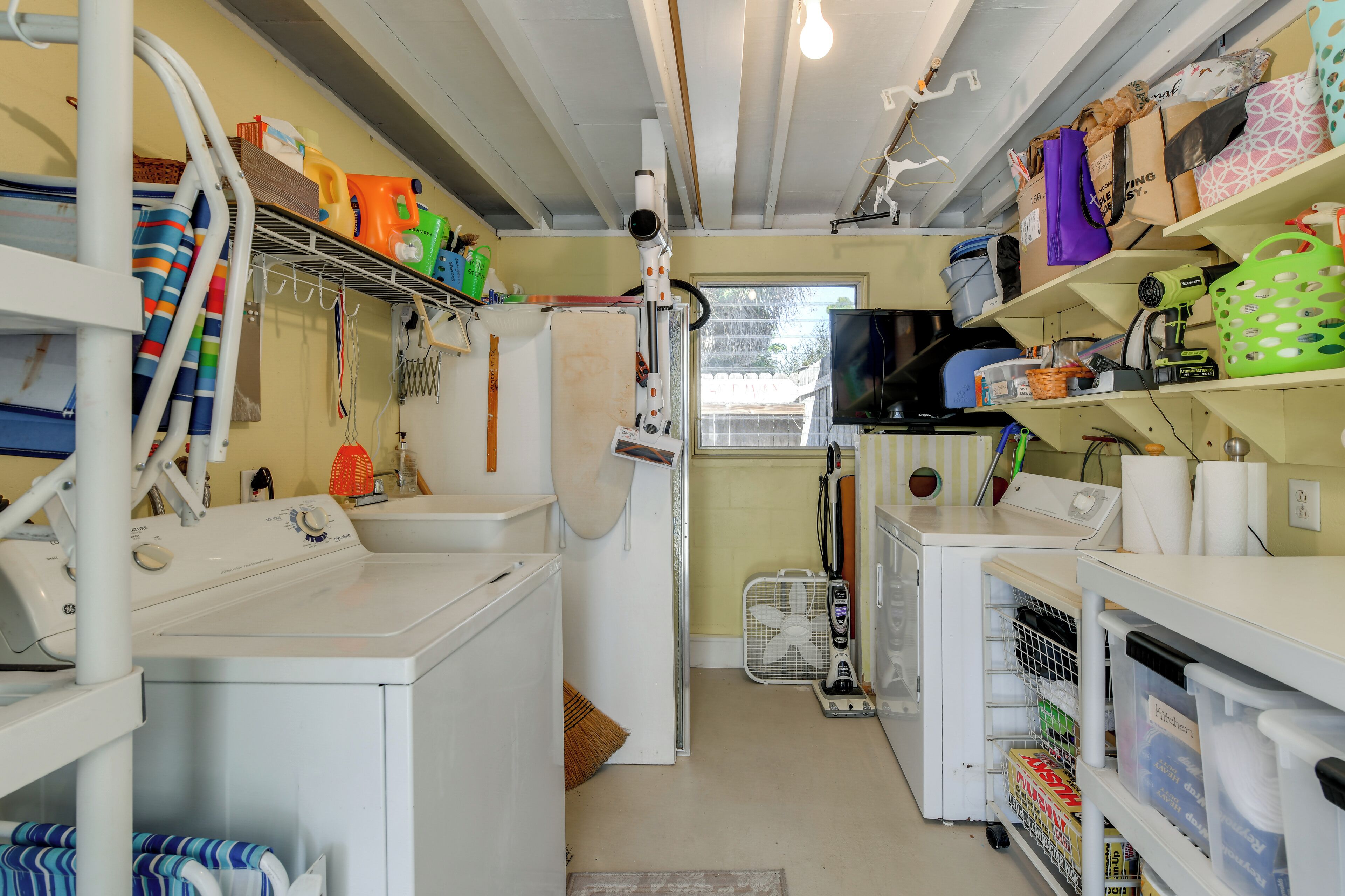 Een wasserette met een wasmachine, droger en diverse schoonmaakmiddelen op planken.