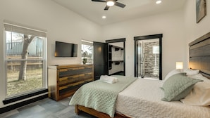 A bedroom with a bed, a dresser, a TV, and a view of the outdoors. - Roo's Hideaway Modern 3BR Near Round Top & A&m! (Somerville)