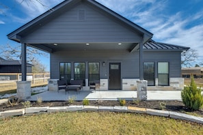 Une maison moderne à deux étages, dotée d’un patio couvert, de piliers en pierre et d’un jardin aménagé.