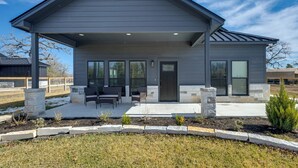 A modern two-story house with a covered patio, stone pillars, and a landscaped garden. - Roo's Hideaway Modern 3BR Near Round Top & A&m! (Somerville)