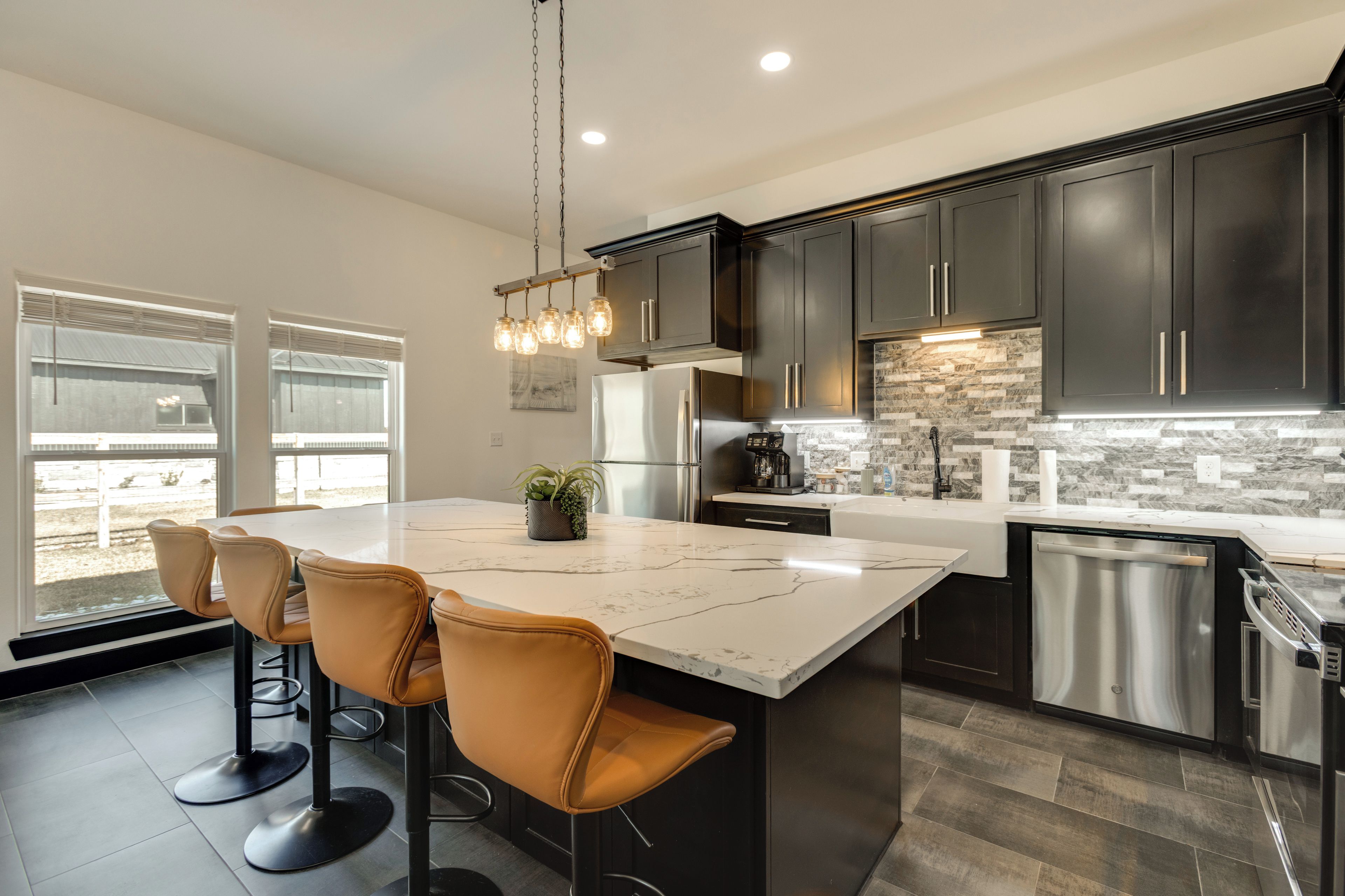 A modern kitchen with dark cabinets, a marble island, and a stainless steel dishwasher.