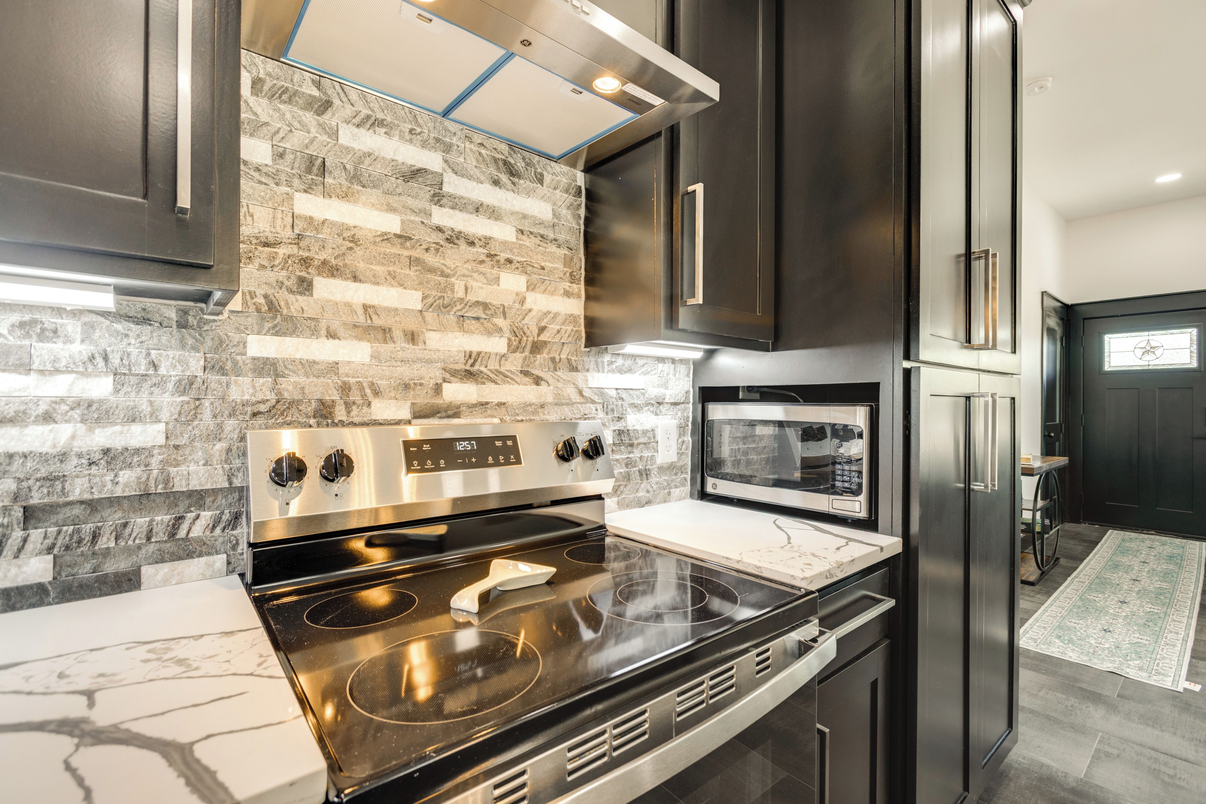 Una cocina moderna con estufa, horno y microondas de acero inoxidable, muebles oscuros y un salpicadero con diseño.