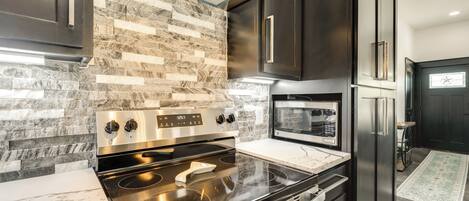 Una cocina moderna con estufa, horno y microondas de acero inoxidable, muebles oscuros y un salpicadero con diseño.