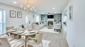 A dining area with a round table, wicker chairs, and a chandelier. There is a sofa and a fireplace in the background. - East Texas Group Getaway! Modern Longview Home (Longview)