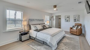 A bedroom with a bed, nightstand, chair, and artwork on the wall. - East Texas Group Getaway! Modern Longview Home (Longview)