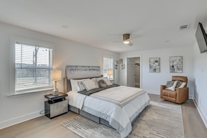 A bedroom with a bed, nightstand, chair, and artwork on the wall. - East Texas Group Getaway! Modern Longview Home (Longview)