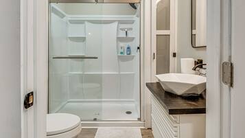 A modern bathroom with a glass-enclosed shower, a white toilet, a sink with a dark countertop, and a mirror above the sink.
