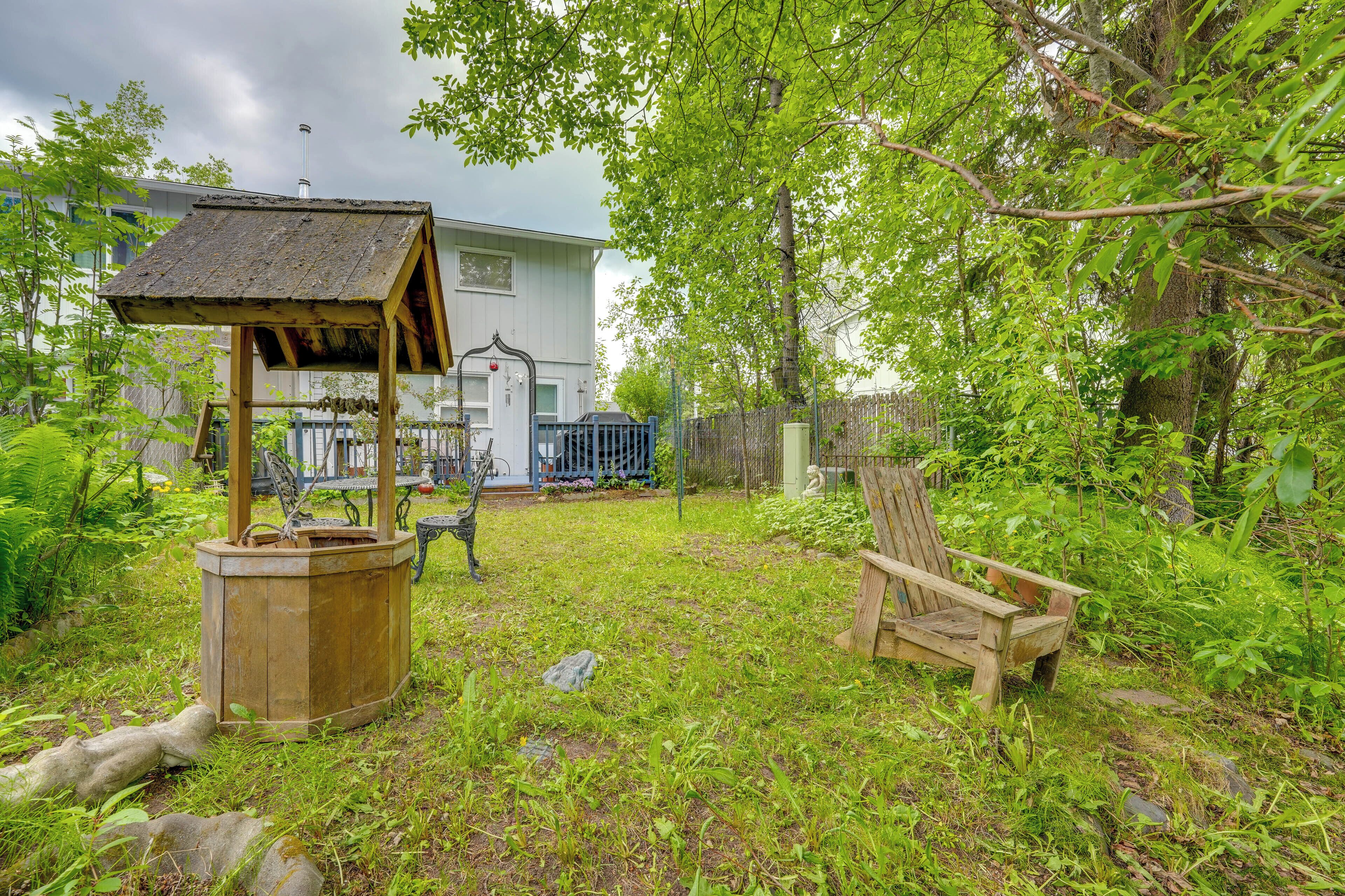 A rustic wooden structure, a bench, and a house in a lush garden.