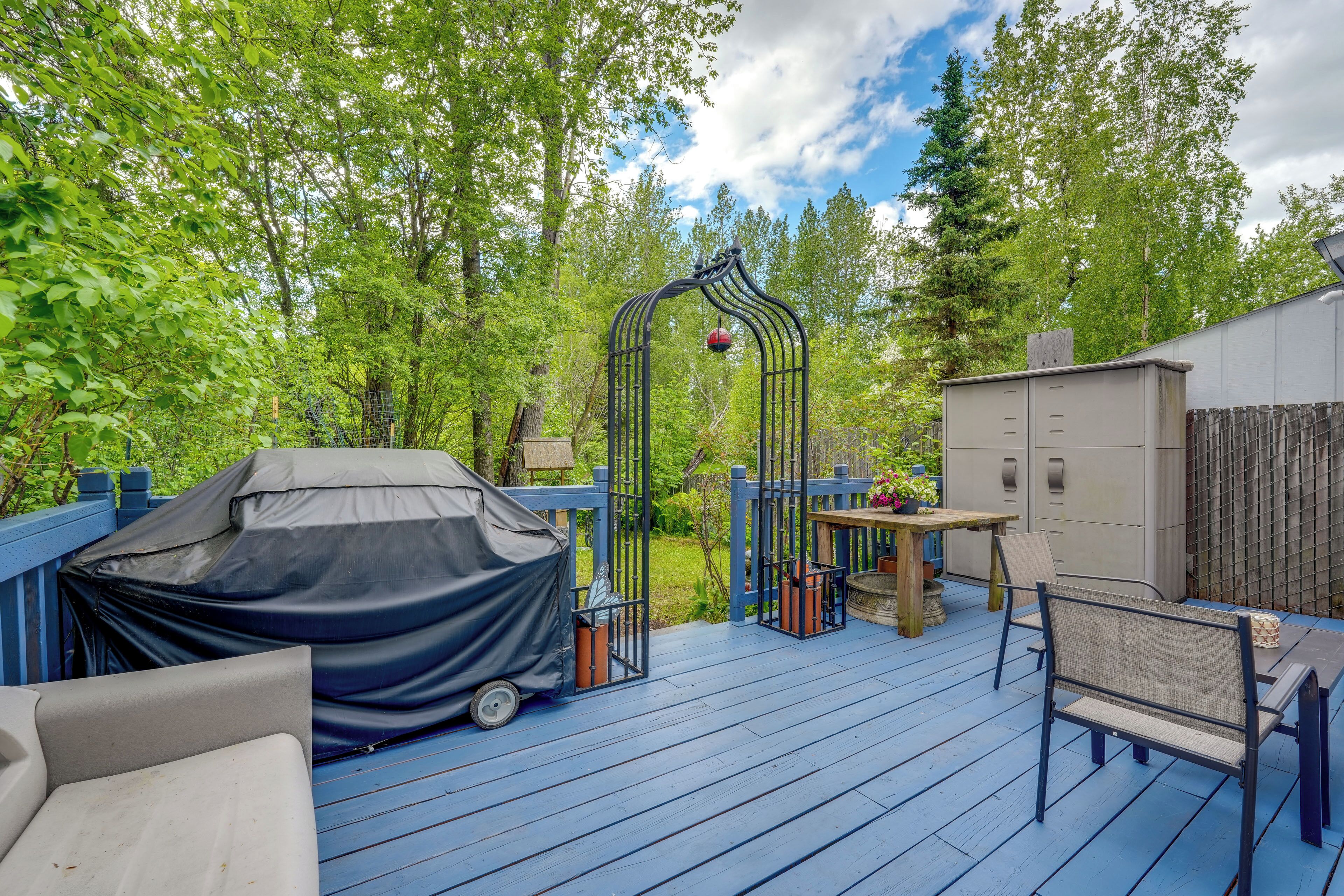 A covered outdoor deck with a table and chairs, surrounded by a wooden fence and trees.