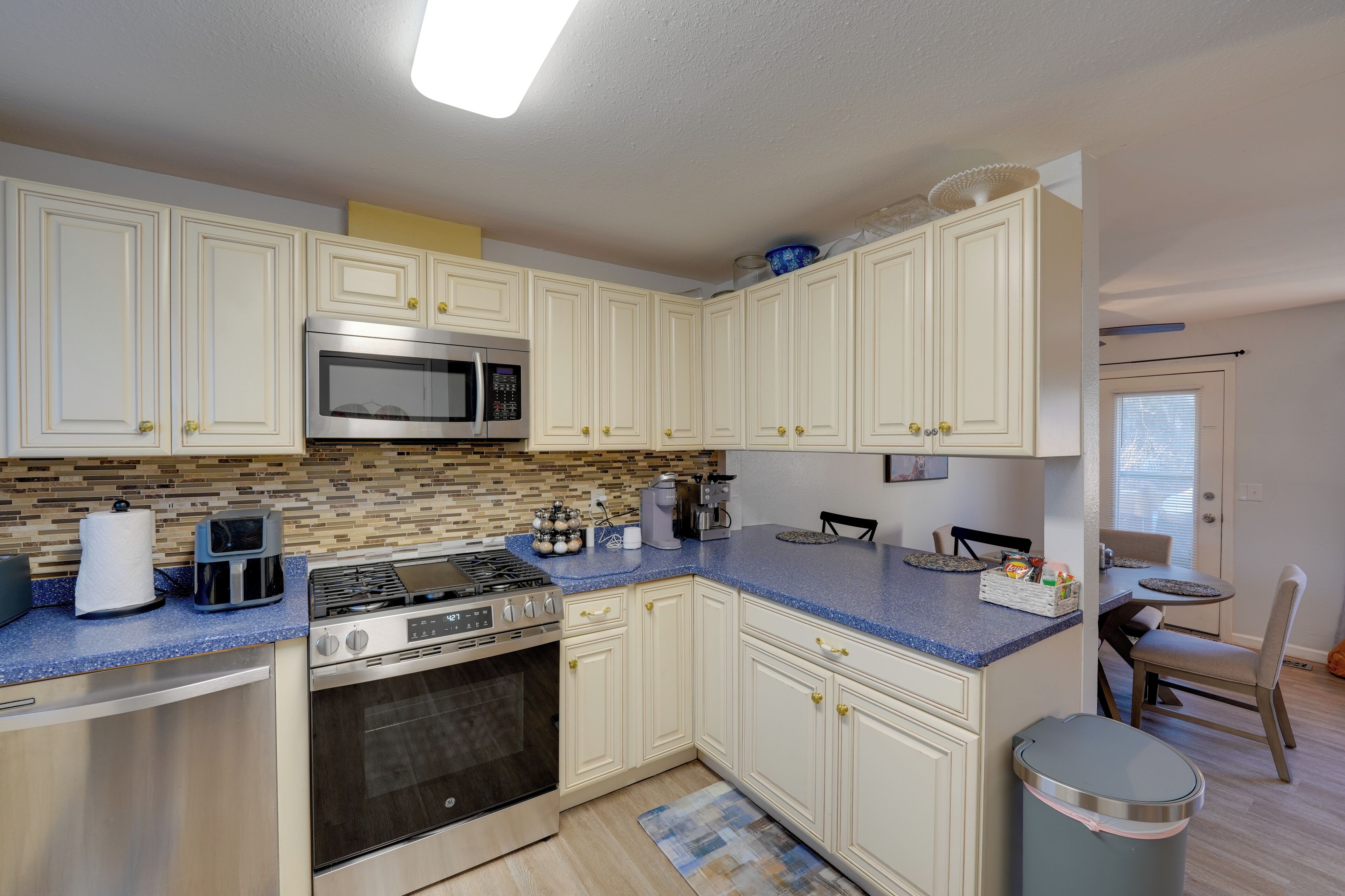 A kitchen with white cabinets, a blue countertop, a microwave, a stove, and a trash can.
