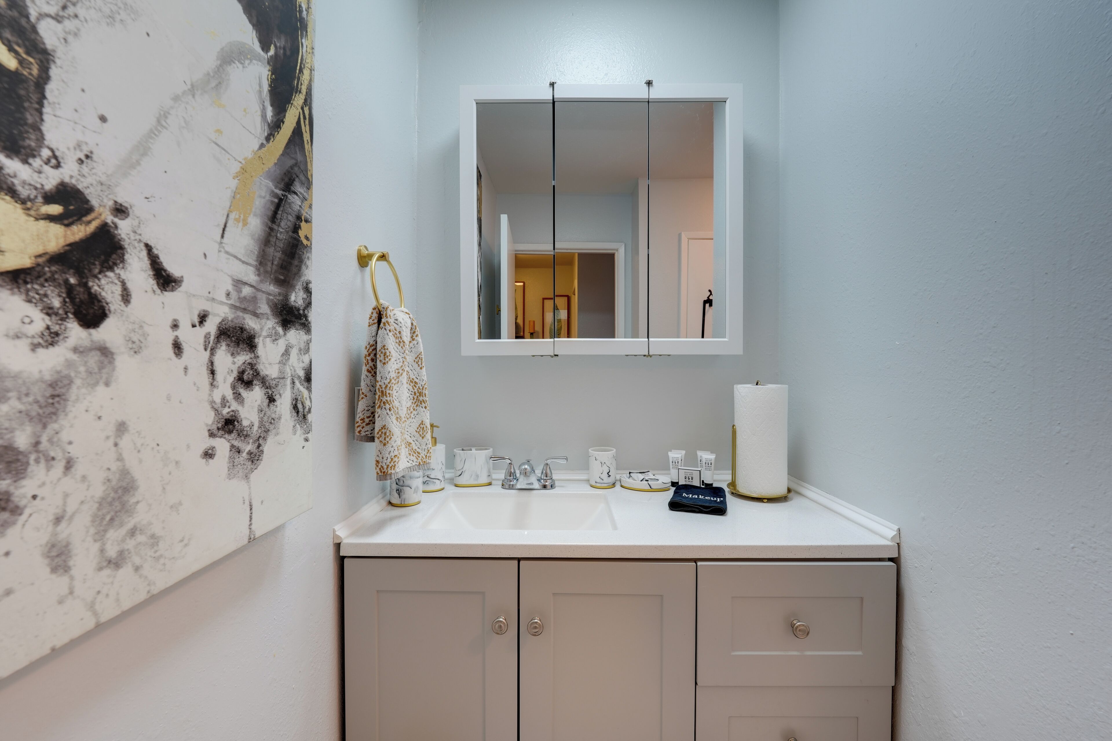 A bathroom with a white sink, a mirror, and a towel hanging on the wall.
